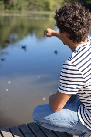 young happy man feeding ducks in the pondの写真素材