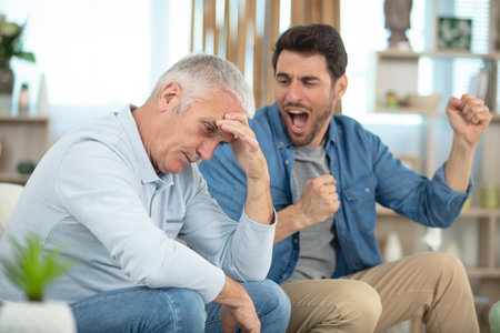 family problems disgruntled father and adult son at homeの写真素材