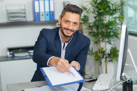 young man doing paperwork at office desk asking for signatureの写真素材