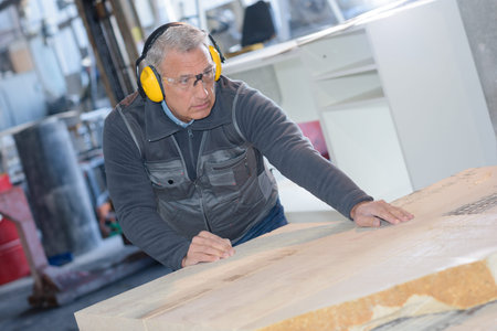 mid adult carpenter using tablesaw to cut wood in workshop
