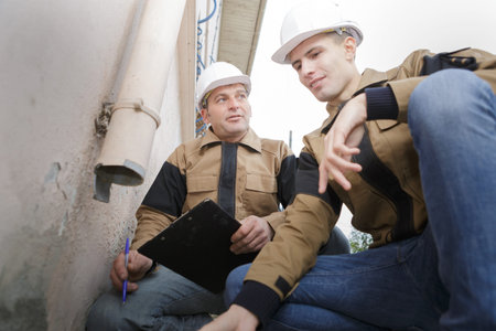 plumber in hardhat maintaining pipes outside of the houseの写真素材