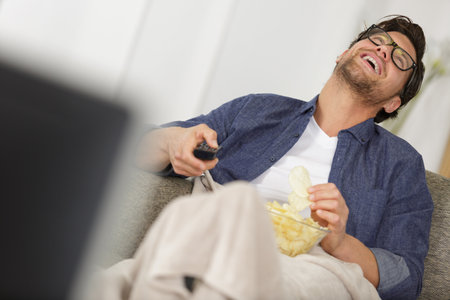 guy with remote control laughingat the televisionの写真素材