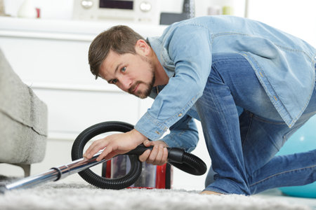 man vacuuming a floor under a bedの写真素材