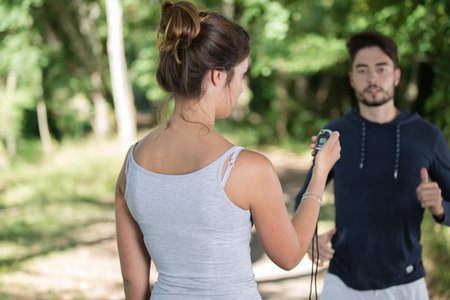 portrait of female coach timing runner in a park