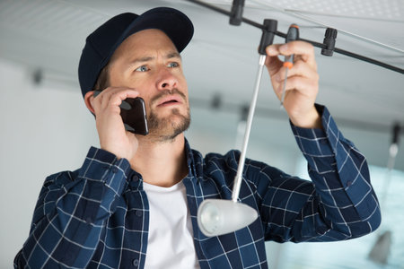 young electrical engineers installing a lamp and talking by phoneの写真素材