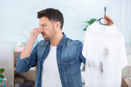man holding a smelly t-shirt and holding his noseの写真素材