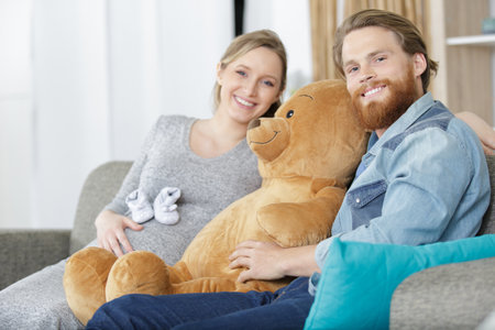 young couple family expecting a baby sitting with big bearの写真素材