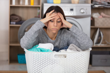 frustrated woman sighs over basket of dirty laundryの写真素材
