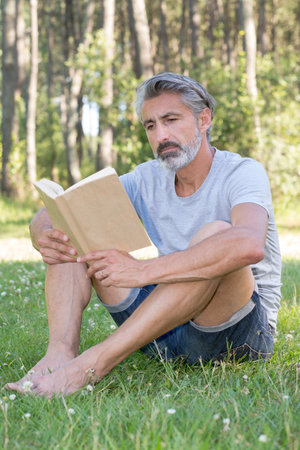 man lyingsitting in the grass reading a bookの写真素材