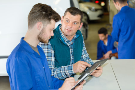 team of mechanics using digital tablet while diagnosing car engineの写真素材