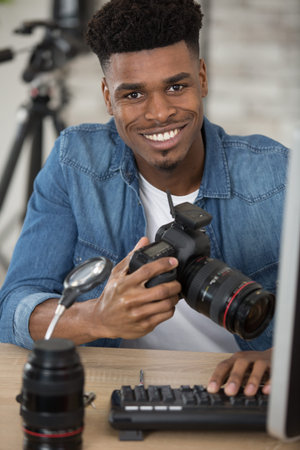 young photographer sitting at table with camera and computer
