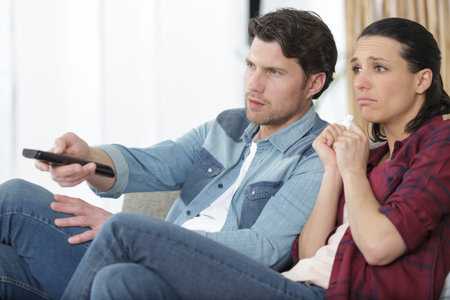 sad couple at home sitting on sofa watching tv