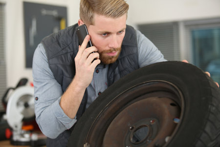 male mechanic looking at wheel and talking on smartphoneの写真素材