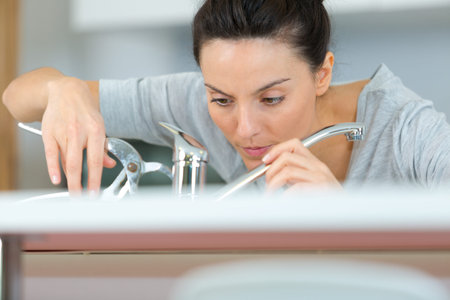 female plumber fitting tap in kitchen sinkの写真素材