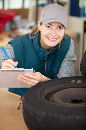 smiling mechanic in coveralls holding tireの写真素材