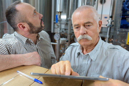 two senior men in brewery using digital tablet