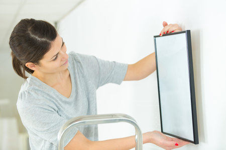 woman positioning picture frame on wall