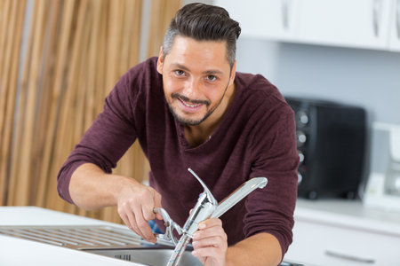 happy man fixing tap in the kitchen at homeの写真素材