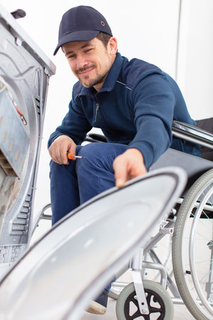 washing machine repairman in wheelchair dismantles machineの写真素材
