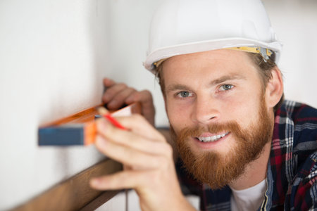 smiling young man measuring wall with level tool
