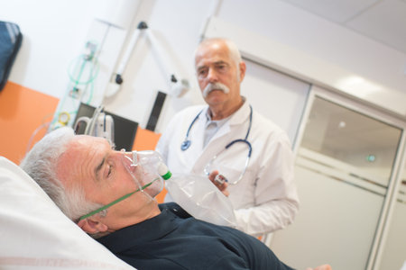 doctor looking at senior male patient inhaling through oxygen mask