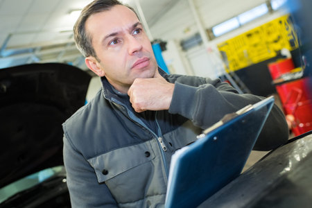 mechanic holding a clipboard thinking