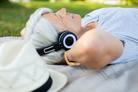 smiling elder lady listening to music on the parkの写真素材