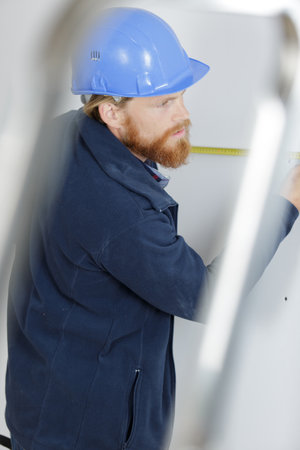 contractor measuring a wall seen through a stepladderの写真素材