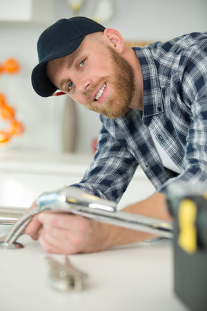 smiling male plumber fixing sink pipe with adjustable wrenchの写真素材