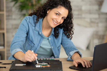 female technician using one laptop while repairing anotherの写真素材