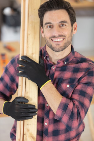 portrait of a smiling carpenter holding wood planksの写真素材