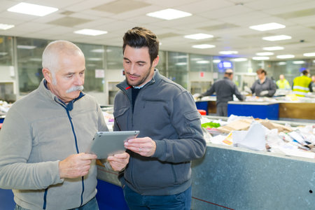 men looking at tablet pc in paper recycling sorting center
