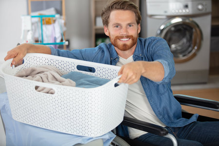 man in wheelchair lifting laundry basket on to ironing boardの写真素材