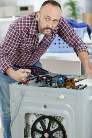 working man plumber repairs washing machine in laundryの写真素材
