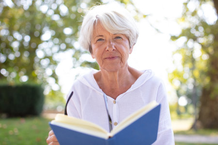 senior woman reading book ugly on the grassの写真素材