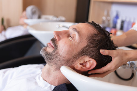 woman applying shampoo and massaging hair of a customerの写真素材