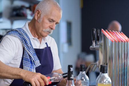 portrait of a senior barista opening bottleの写真素材
