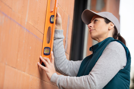 woman bricklayer holding a spirit level on a brick wallの写真素材