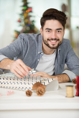 handsome romantic guy is smiling while wrapping a presentの写真素材