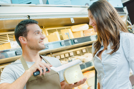 Shop assistant asking customer where to cut chunk of cheeseの写真素材
