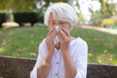adult woman is sitting in park and blowing noseの写真素材