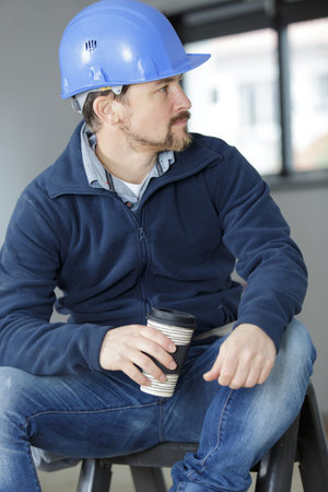 smiling construction worker in helmet drinking coffee