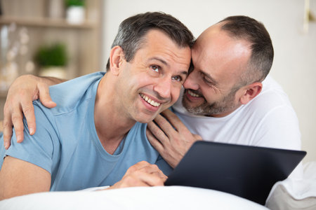 gay couple lying on bed and using laptop at homeの写真素材