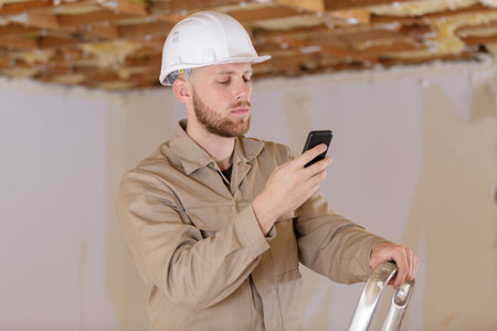 young man builder in hard hat using mobile phone
