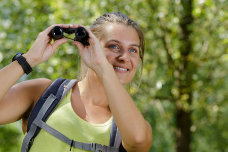 smiling young female hiker with binocularsの写真素材