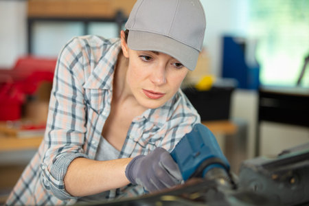 female workerusing power-tool on car bodywork