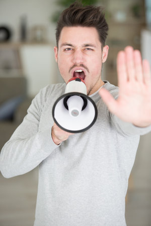young man holding a megaphone shouting and waving his handの写真素材