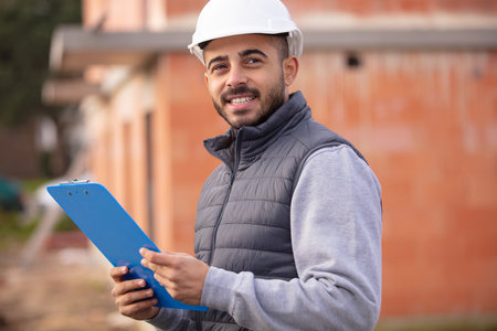 male construction inspector checking outdoor building holding listの写真素材