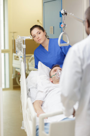 female nurse wheeling male patient along hospital corridorの写真素材