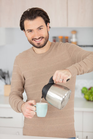 young elegant man pouring tea into cupの写真素材